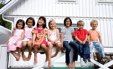 Gruppe barn sitter på gjerde foran hus.